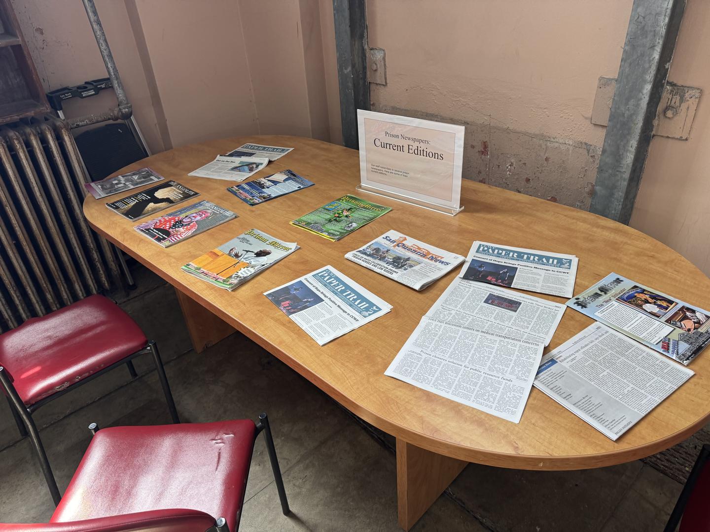 A table spread with current prison newspapers and magazines, laid out beside a card reading “Prison Newspapers: Current Editions”