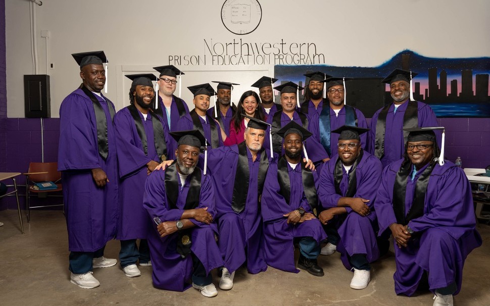 Graduates in purple caps and gowns, smiling beneath a hand-painted Northwestern Prison Education Program mural